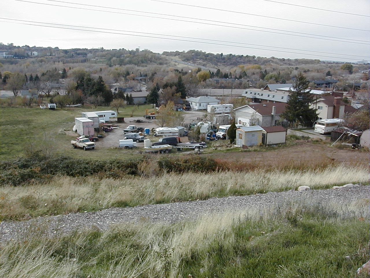 A vacant lot filled with old cars and trailers surrounded by tall grass.